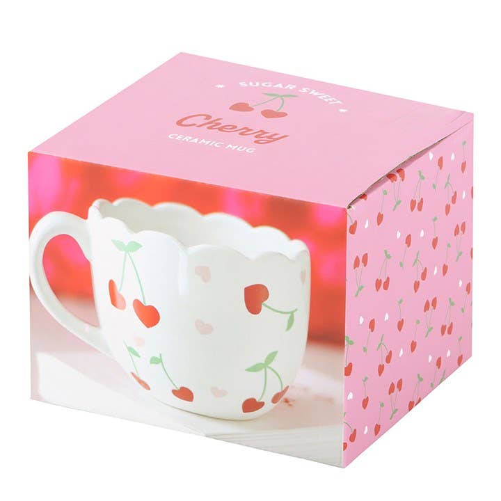 A close-up of a box with a white mug with a scalloped rim. The mug is decorated with small red cherries with green stems and pink hearts.