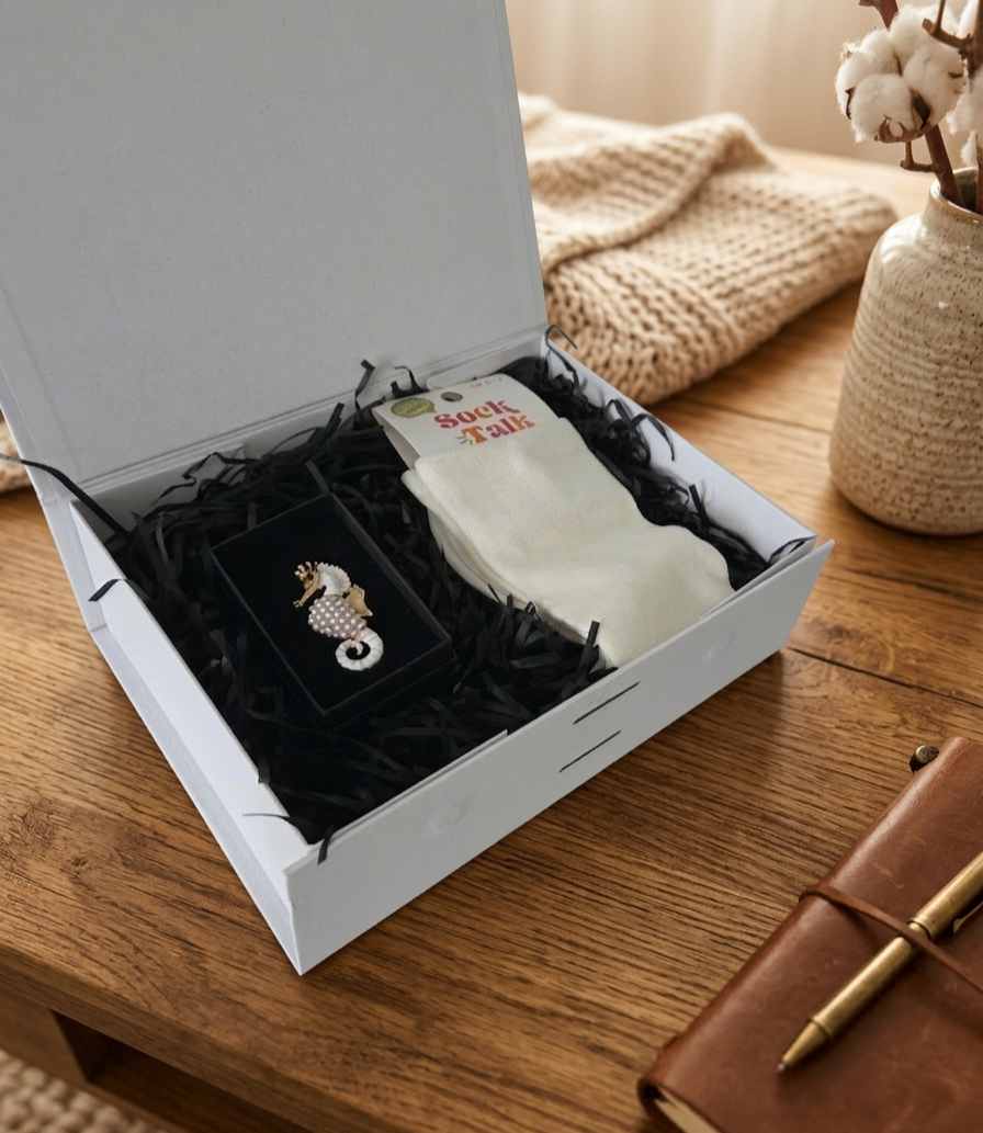 White gift box with a seahorse brooch and bamboo socks on a wooden surface