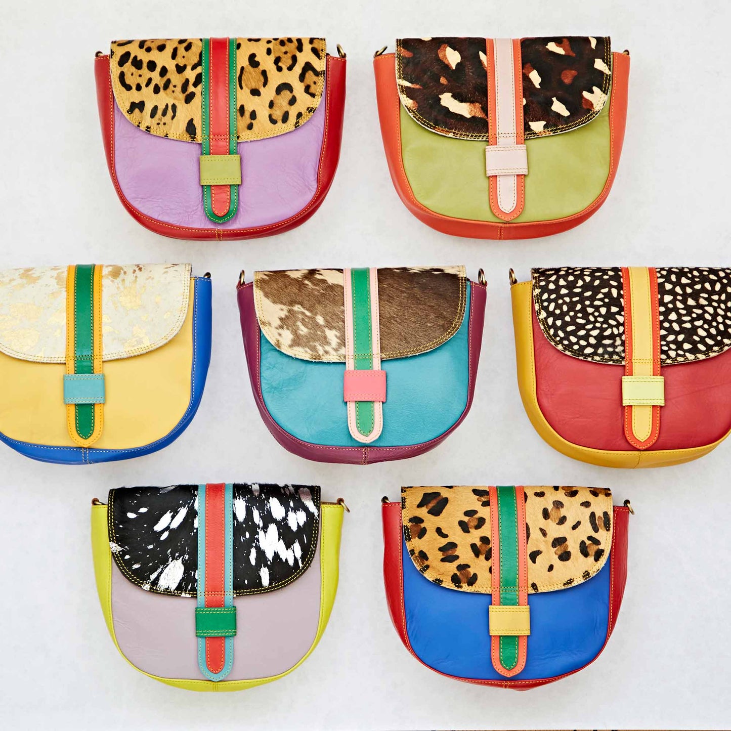 Colourful handmade recycled leather crossbody bags with animal print accents and vibrant designs arranged in three rows on a light background. 
