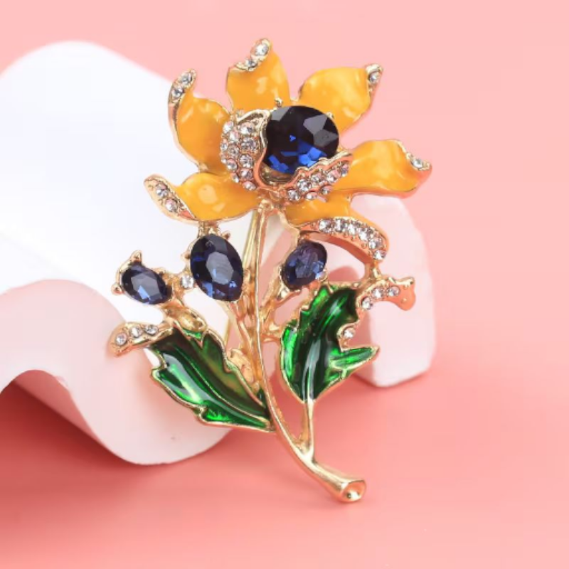 Floral brooch with yellow petals, blue stones, and green leaves on a pink background