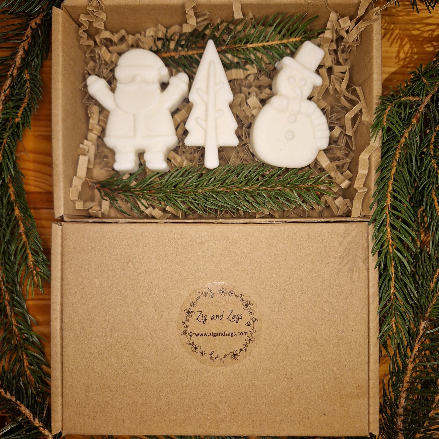 Christmas Gift Box with three white Christmas themed wax melts displayed on a wooden surface with pine branches