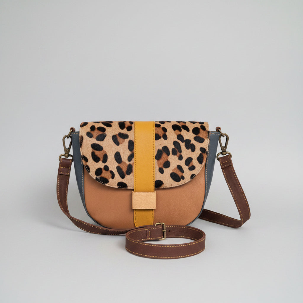 Handmade recycled leather crossbody bag in brown, yellow and leopard print patchwork design with adjustable strap on a white background.
