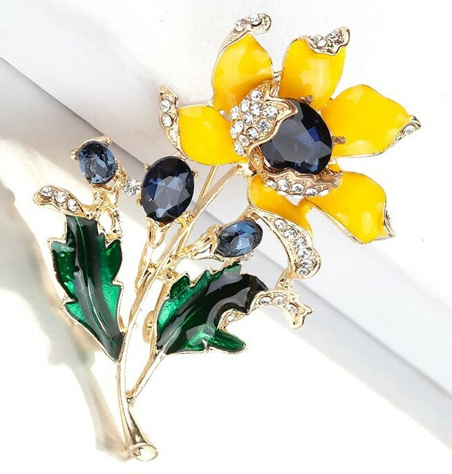 Brooch with yellow flower, green leaves, and blue stones on a white background