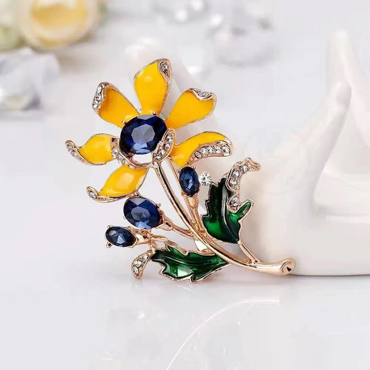 Yellow enamel flower brooch with blue crystals on white background