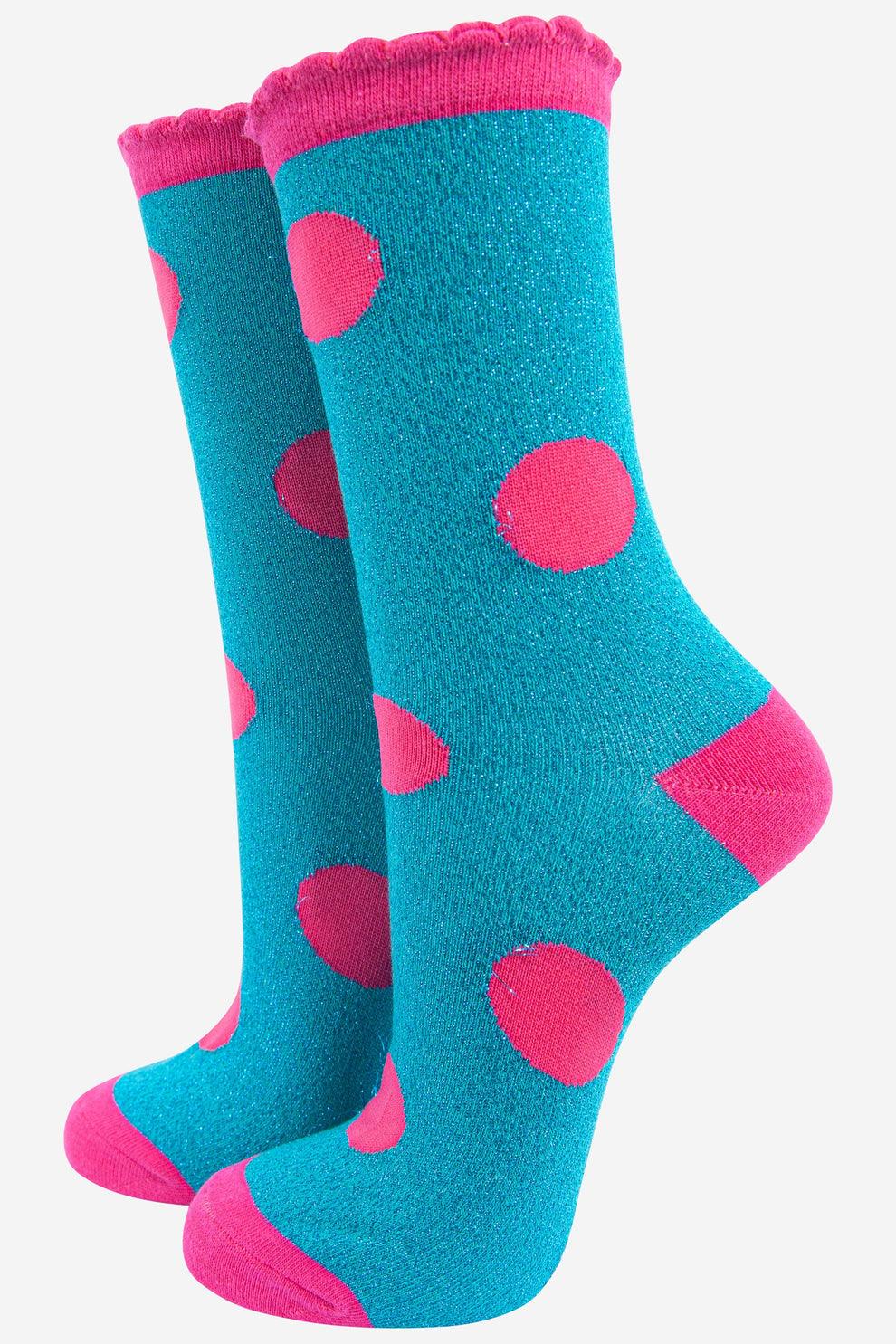 A pair of turquoise socks with large pink polka dots, pink heels and toes, and a scalloped pink cuff.
