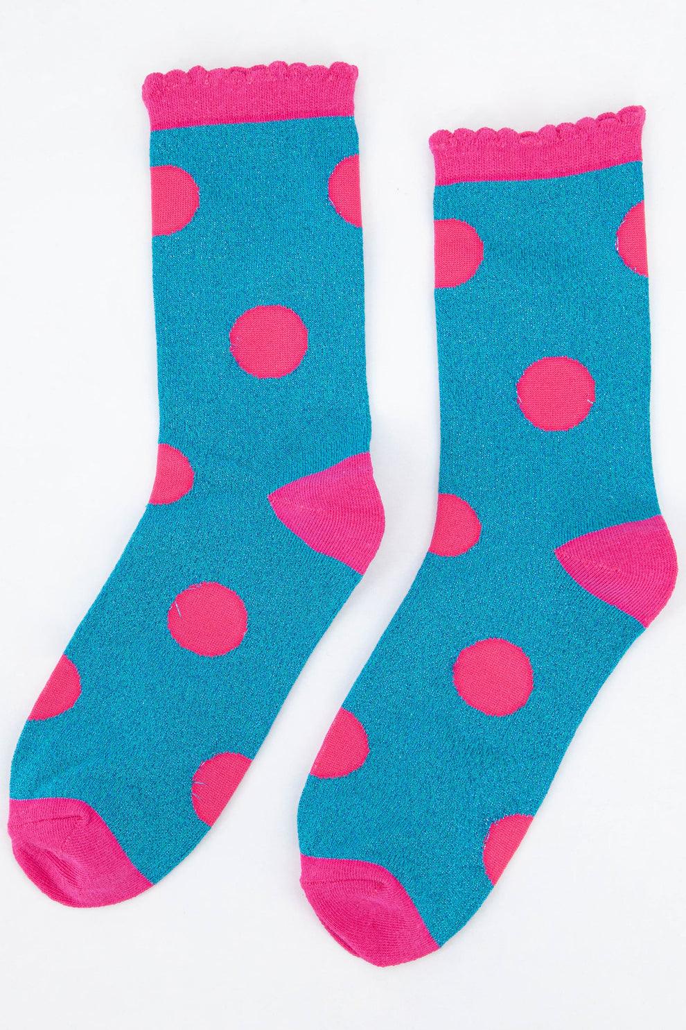 Flat lay of a pair of turquoise socks with large pink polka dots, pink heels and toes, and a scalloped pink cuff.
