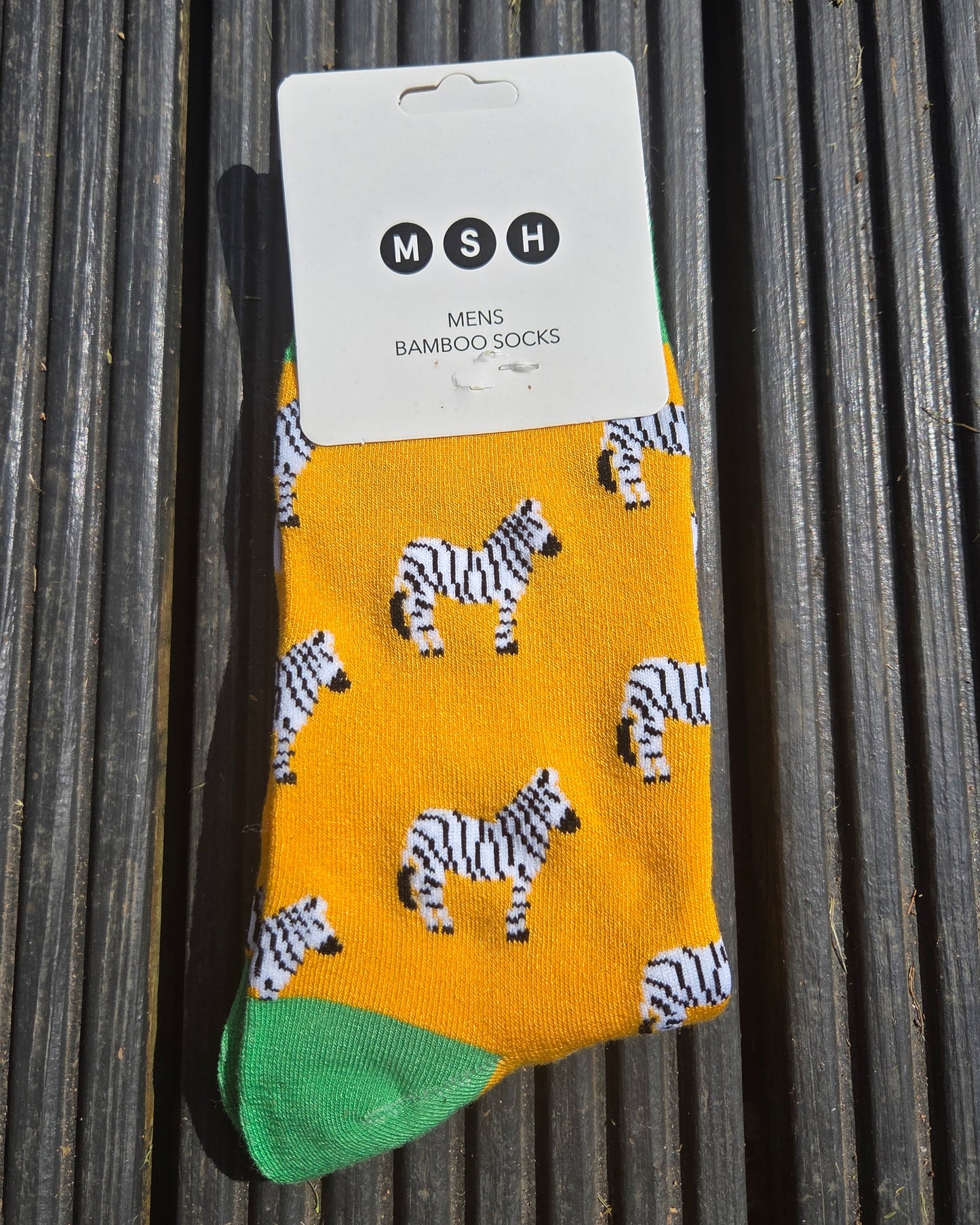 Packaging of socks with zebra pattern on a yellow background, displayed on a wooden surface.